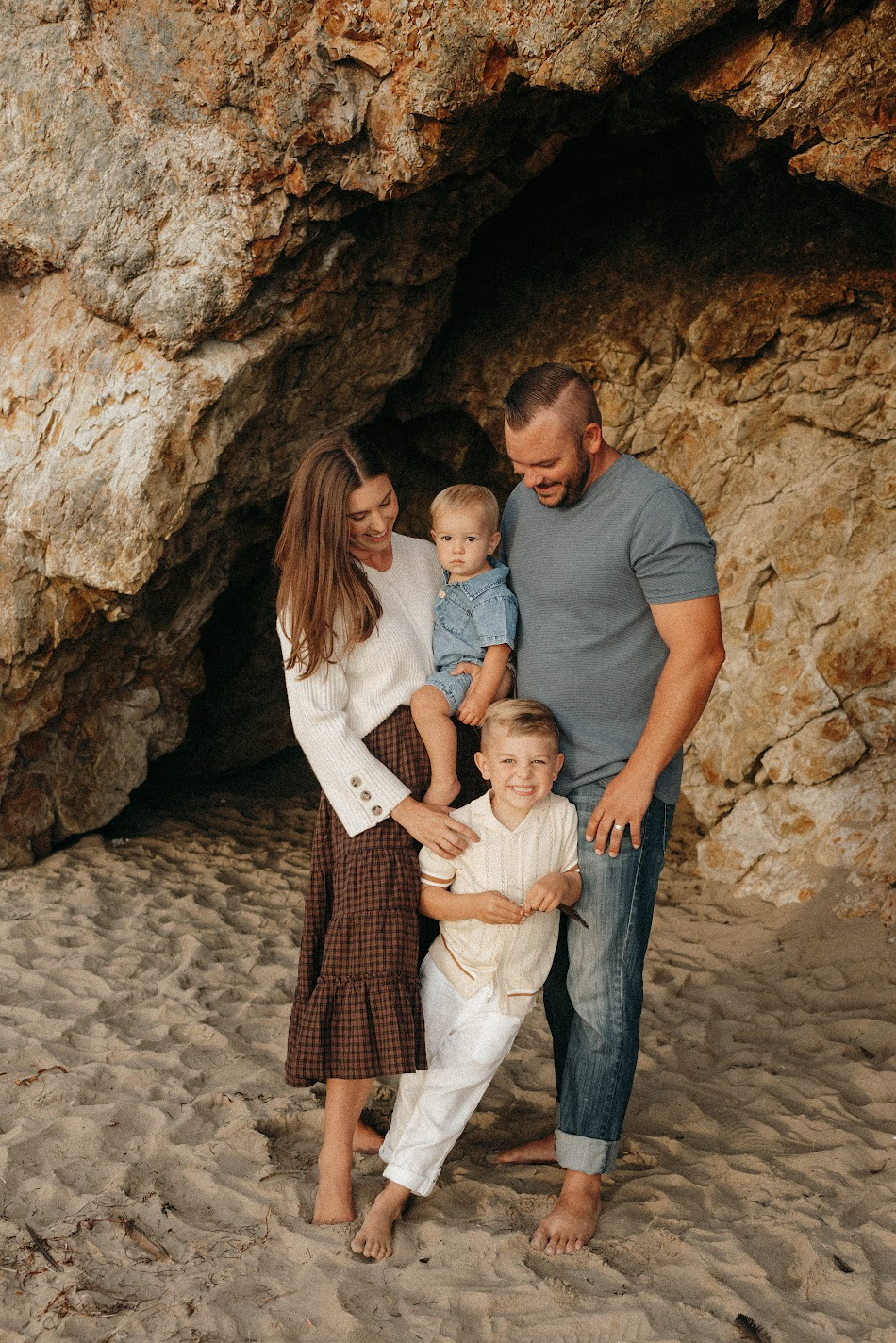 Michelle's family of four with two young boys nestled inside a sandstone sea cave